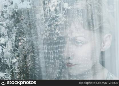 Face of young woman behind transparent cloth with bouquet of dried flowers
