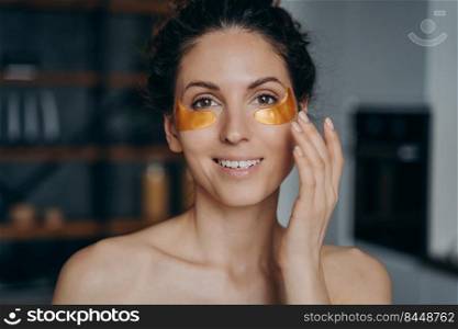 Face of young woman which applies collagen eye patches. Portrait of happy european girl doing spa procedures. Golden anti wrinkle patches. Cosmetics, skincare and anti age beauty routine.. Face of young woman which applies collagen eye patches. Portrait of happy girl doing spa procedures.