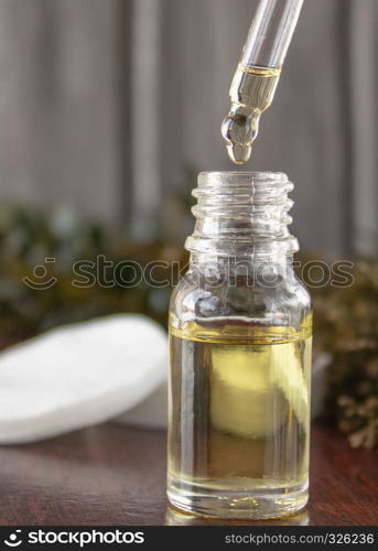 Face oil in a glass bottle on a dark background. Liquid oil drips from the pipette into the jar.. Face oil in a glass bottle on a dark background.