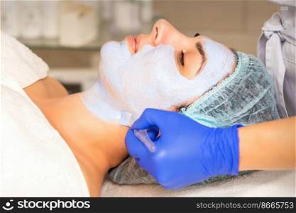 Face peeling at the beautician. Facial treatment. The beautician applies a cleansing face mask to the female patient. Face peeling at the beautician. Facial treatment. The beautician applies a cleansing face mask to the female patient.