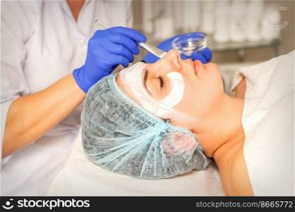 Face peeling at the beautician. Facial treatment. The beautician applies a cleansing face mask to the female patient. Face peeling at the beautician. Facial treatment. The beautician applies a cleansing face mask to the female patient.