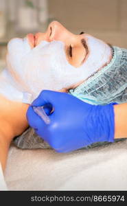 Face peeling at the beautician. Facial treatment. The beautician applies a cleansing face mask to the female patient. Face peeling at the beautician. Facial treatment. The beautician applies a cleansing face mask to the female patient.