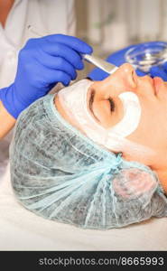 Face peeling at the beautician. Facial treatment. The beautician applies a cleansing face mask to the female patient. Face peeling at the beautician. Facial treatment. The beautician applies a cleansing face mask to the female patient.