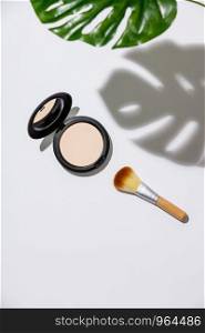 Face powder and brush for makeup and monstera leaves on a white background, flat lay. Face powder and brush for makeup, flat lay
