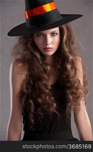 face shot of a young and beautiful girl dressed up for halloween with a huge black witch hat looking straight into the cam