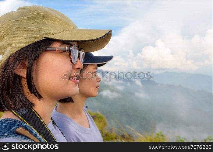 Face two young women hiker, mother and daughter smiling happily while looking beautiful landscape nature of mountain range and sky at Phu Chi Fa Forest Park, Chiang Rai, Thailand