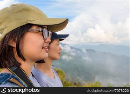 Face two young women hiker, mother and daughter smiling happily while looking beautiful landscape nature of mountain range and sky at Phu Chi Fa Forest Park, Chiang Rai, Thailand