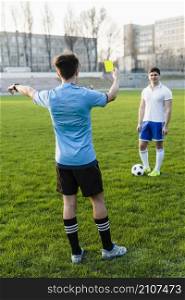 faceless referee showing yellow card sportsman