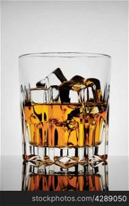 Faceted amber glass with whiskey and ice on gray background