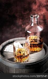 Faceted glass and dusty decanter of brandy on a wooden barrel