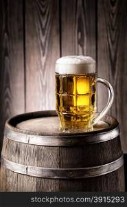 Faceted glass of light beer with a thick foam on an old wooden barrel. Faceted glass of light beer with a thick foam