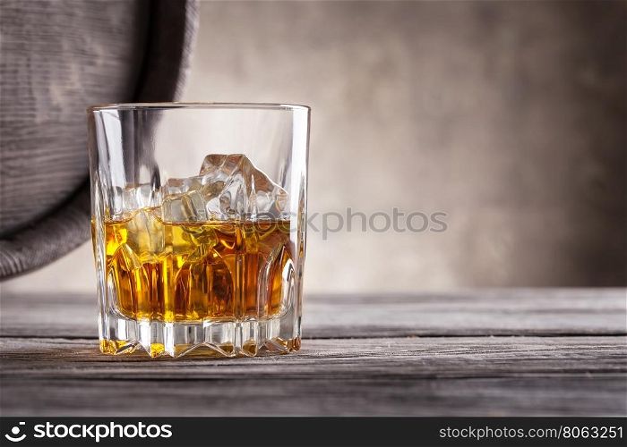 Faceted glass of whiskey and the angle of wooden barrels on a dark background. Faceted glass of whiskey and the angle of wooden barrels