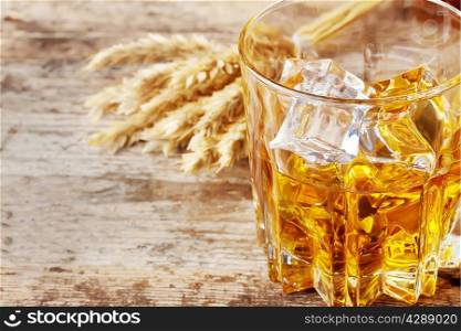 Faceted glass of whiskey with ice and ears on wooden table