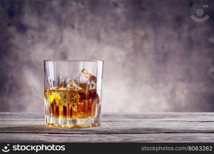 Faceted glass of whiskey with ice cubes on a wooden table. Faceted glass of whiskey with ice cubes