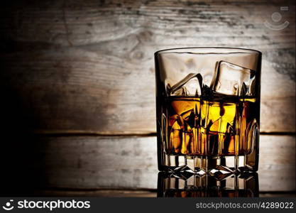 Faceted glass of whiskey with ice on a wooden background
