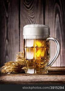 Faceted mug of light beer with foam and ears on the wooden background. Faceted mug of light beer with foam and ears
