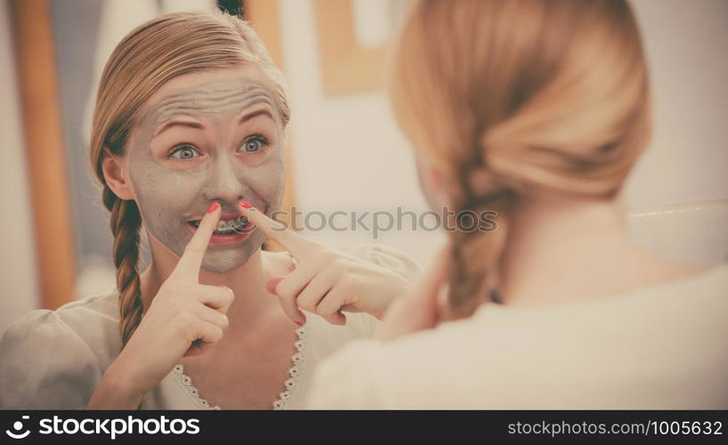 Facial dry skin and body care, complexion treatment at home concept. Happy young woman having grey mud mask on her face making funny expession.. Happy young woman having mud mask on face