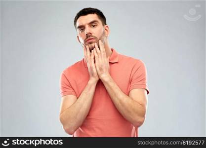 facial expression and people concept - young man in polo t-shirt touching his face over gray background. young man touching his face over gray background