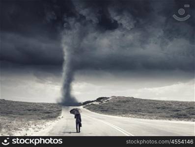 Facing challenges. Back view of businessman with umbrella and suitcase facing tornado