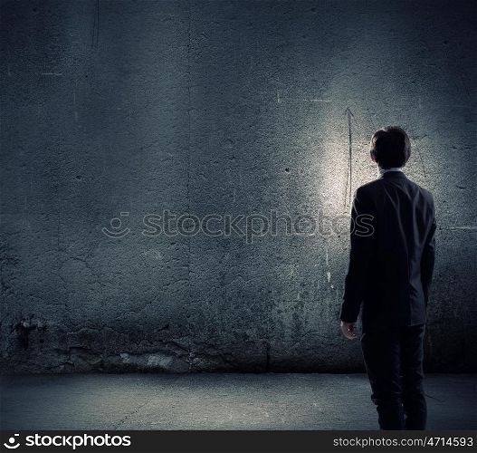 Facing challenges. Rear view of businessman looking at blank cement wall
