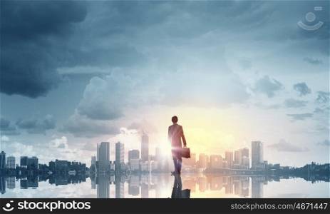 Facing new day. Businessman standing with back and looking at sunrise above city
