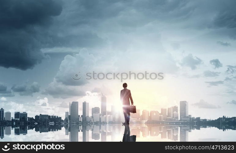 Facing new day. Businessman standing with back and looking at sunrise above city