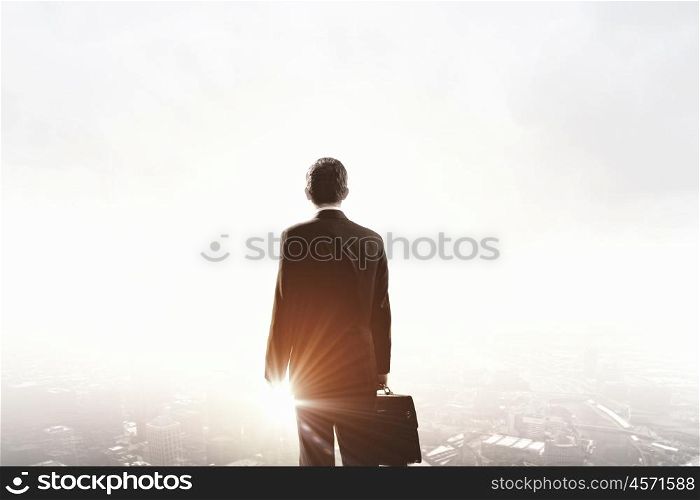 Facing new day. Rear view of businessman looking at sunset above city