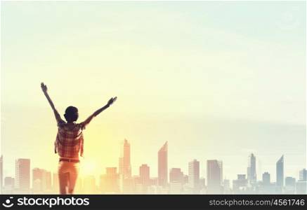 Facing new day. Rear view of girl with hands up facing sunrise abone city