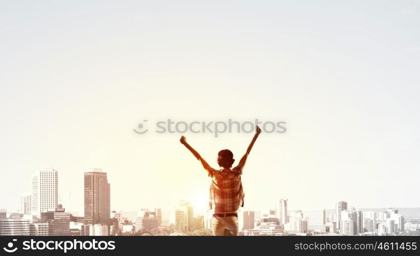 Facing new day. Rear view of girl with hands up facing sunrise abone city