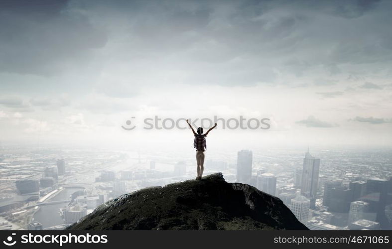 Facing new day. Rear view of girl with hands up facing sunrise abone city