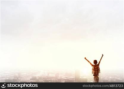 Facing new day. Rear view of girl with hands up facing sunrise abone city