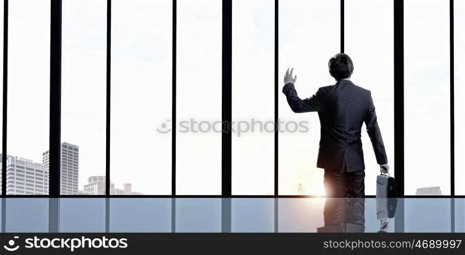 Facing next successful day. Back view of businessman looking on sunrise in office window and gesturing with hand