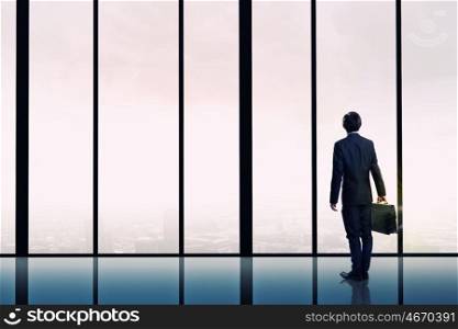 Facing next successful day. Back view of businessman looking on sunrise in office window