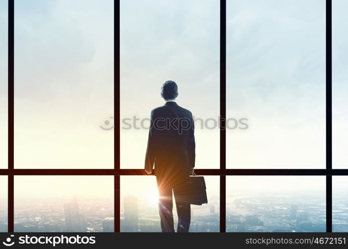 Facing next successful day. Back view of businessman looking on sunrise in office window