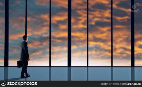 Facing next successful day. Back view of businessman looking on sunrise in office window