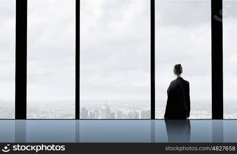 Facing next successful day. Back view of businesswoman looking in office window