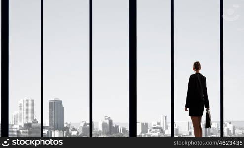 Facing next successful day. Back view of businesswoman looking on sunrise in office window