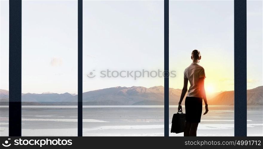 Facing next successful day. Back view of businesswoman looking on sunrise in office window