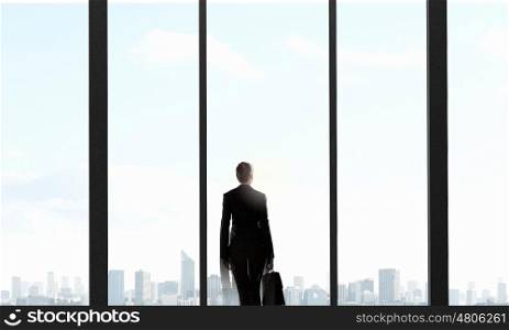 Facing next successful day. Back view of businesswoman with handbag looking in office window