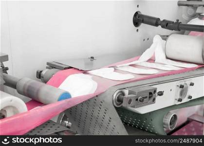 factory and equipment for the production of female sanitary napkins. women hygiene pads on a conveyor belt closeup. production of women’s sanitary napkins