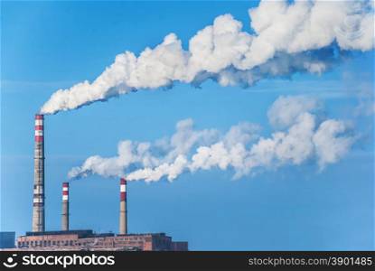Factory chimneys with white smoke against a blue sky