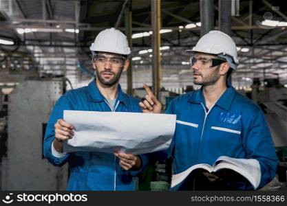 Factory Engineer or mechanical worker with white safety helmet holding the manual and checking on production in a factory. Industrial,Warehouse Heavy Mechanic, Engineering Concept.