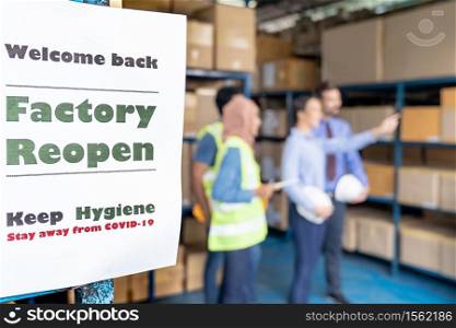 Factory reopen signage with warehouse manager and worker meeting in background after city lockdown from COVID-19 coronavirus pandemic in warehouse distribution center environment.