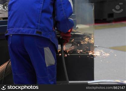 Factory worker in working clothes welding metal construction.