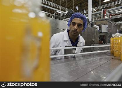 Factory worker standing by production line of juice bottles
