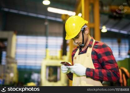 Factory worker with plaid shirt, helmet, safety using corporate application on smartphone to report work progress to manager. Working at night shift to finish production target. Manufacture industry.
