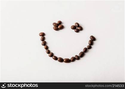 Fair trade roasted organic coffee beans arranged as a smile on white background - Concept of caffeine addiction, breakfast, energy or morning happiness - Coffee shop, cafe and restaurant decor.