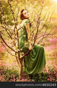 Fairy-tail forest nymph, beautiful sexy woman at spring garden, wearing long dress, sitting on blooming tree, vintage dreamy fashion style