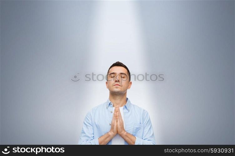 faith in god, religion and people concept - happy man with closed eyes praying under ray of ligh over gray background