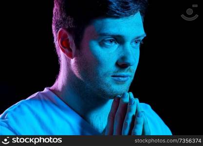 faith, religion and people concept - close up of young man praying god in dark room with ultra violet neon lights. man praying god over ultra violet neon lights